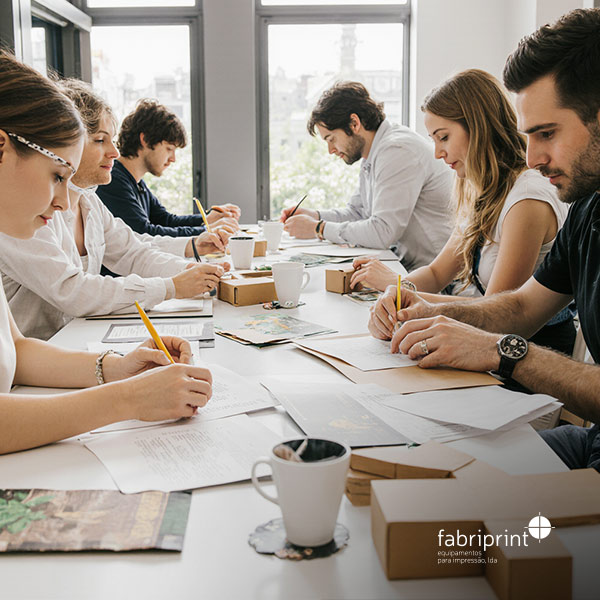 Equipa de design a trabalhar em esboços e protótipos de embalagem numa reunião criativa. Logótipo Fabriprint visível.